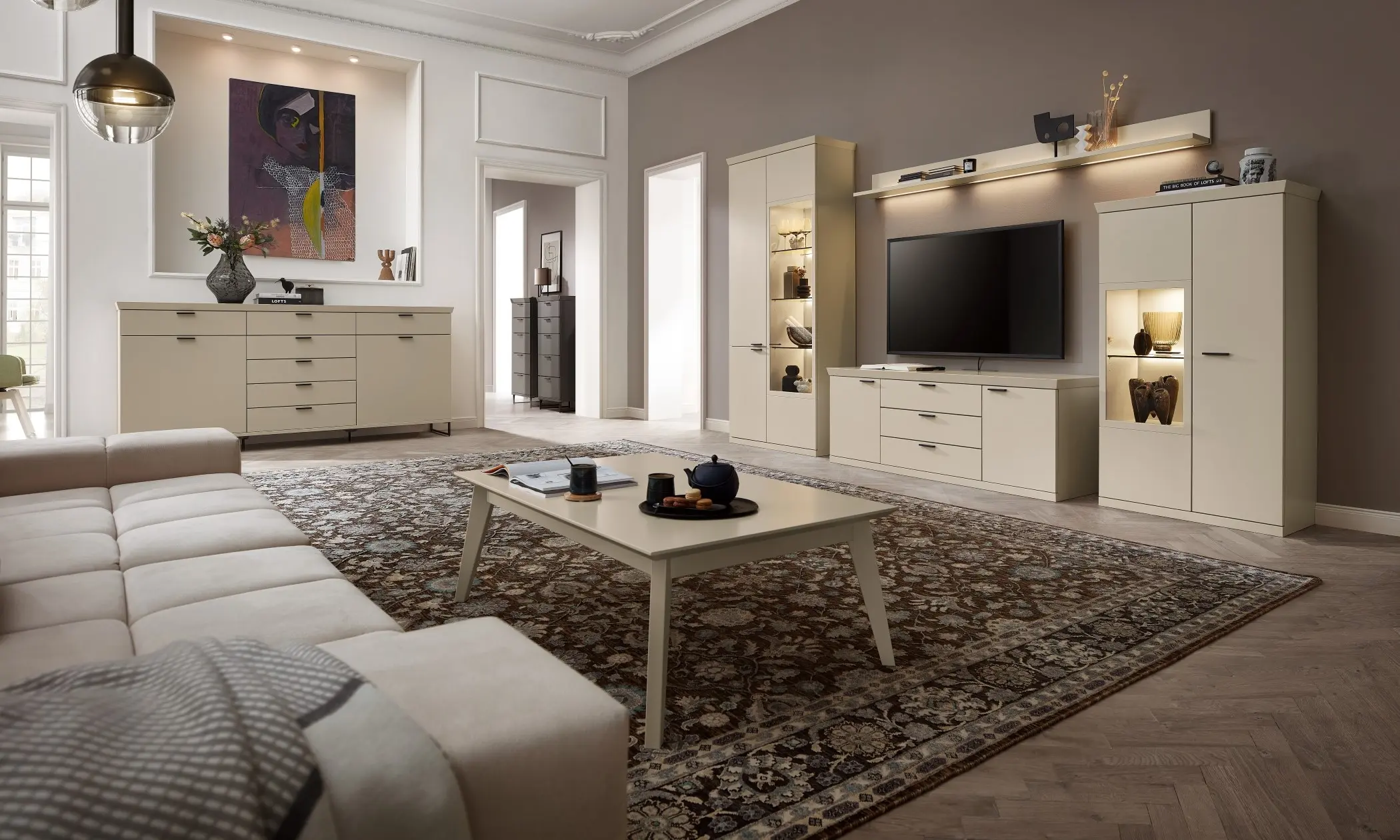 Sie sehen ein schönes Wohnzimmer in der Farbe creme, mit beleuchteten Vitrinen und Lowboard wie auch Sideboard. Sie haben werden verziert durch einen schönen zeitlosen Kranz als Abdeckboden